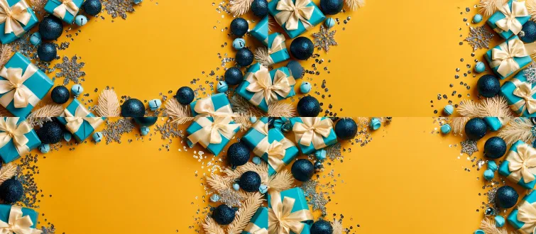 top-down flat lay shot, bright solid mustard yellow background, large blank empty negative space in the center of the frame, christmas festive decorations arranged only along the left and right edges, turquoise wrapped gift boxes tied with cream satin ribbons, dark blue glitter christmas baubles, silver snowflake ornaments, tiny silver sequin confetti dots, mini light blue bell ornaments, pale frosted pine needle branches, vibrant high saturation color contrast, soft even studio lighting, clean minimalist festive aesthetic, wide banner composition, ultra sharp detail