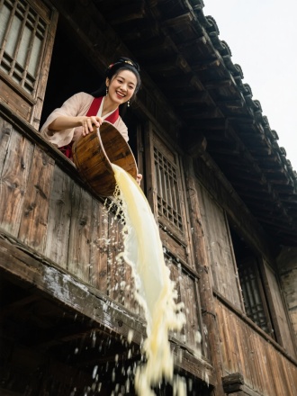 武侠大电影风格，仰拍镜头，古代老旧木楼，绝美的潘金莲在楼上窗口手持一倾斜木盆，木盆里装着淡黄色液体，从楼上窗口往下一泼，液体动态模糊，潘金莲表情笑吟吟。